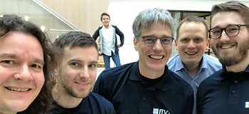 Several men in blue shirts and glasses smile together, creating a cheerful and friendly atmosphere.