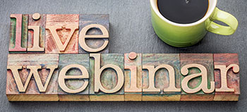 Wooden letter blocks spelling out 'live webinar' next to a green cup filled with black coffee on a gray surface