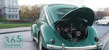 Vintage green Volkswagen Beetle parked on a street with its rear engine hood open, logo ‘365 Stadtwerk’ visible in the corner.