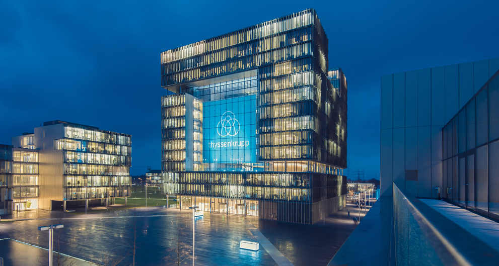 Modern office buildings at night with illuminated windows and a large glass facade displaying