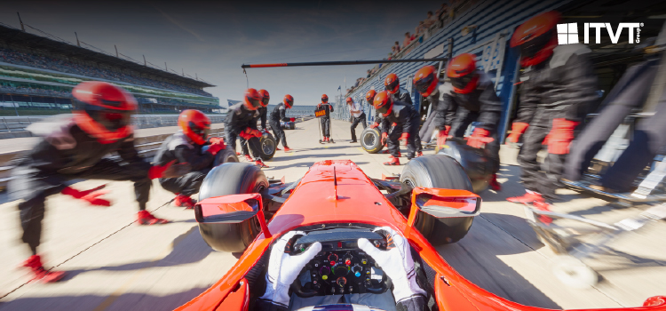 A group of people dressed in red and black uniforms is working together on a race car in a pit area