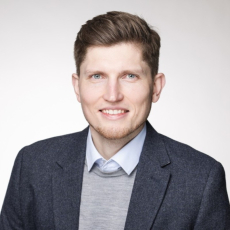 Professional portrait-style photo of a person wearing a dark blazer, light blue shirt, and grey sweater, used for ITVT corporate materials.
