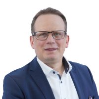 A professional portrait of a person wearing a navy blue suit jacket and a white dress shirt, photographed against a clean white background. Image prepared for ITVT corporate branding and materials.