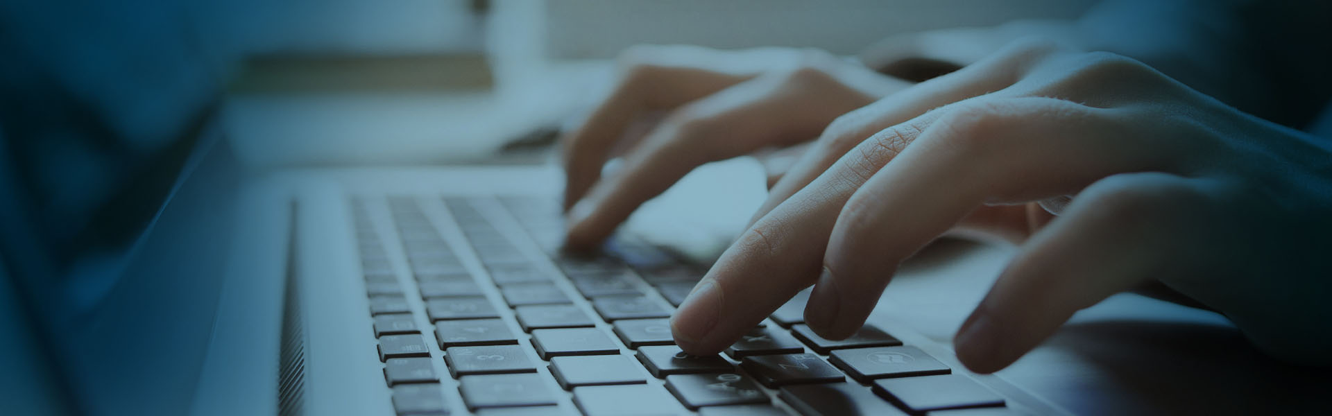 Eine Nahaufnahme von Händen, die auf einer Laptop-Tastatur tippen, mit einem sanften blauen Lichtüberzug, der eine konzentrierte und professionelle Atmosphäre schafft.